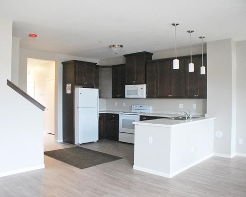an empty kitchen with white appliances and dark cabinets