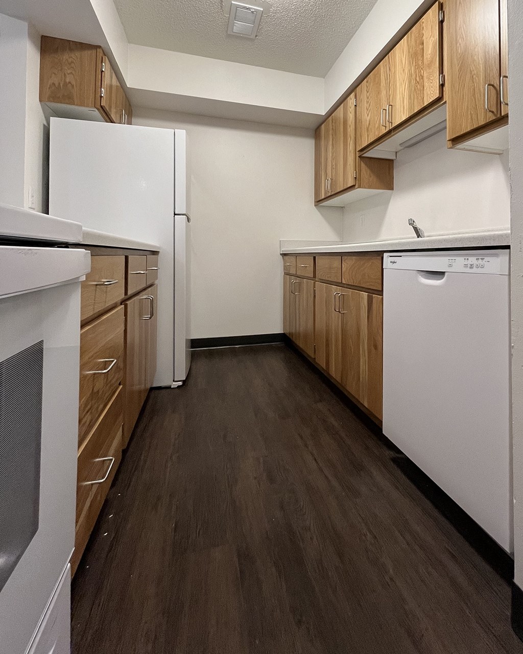 an empty kitchen with white appliances and wooden cabinets