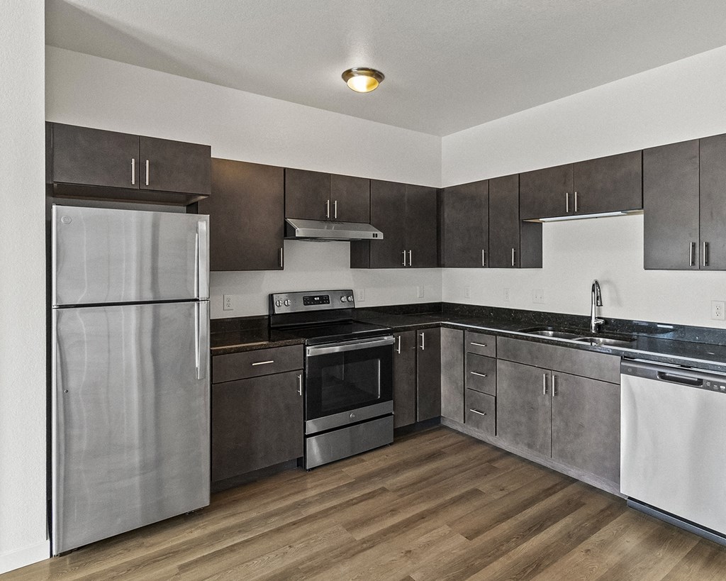 an empty kitchen with stainless steel appliances and wooden floors