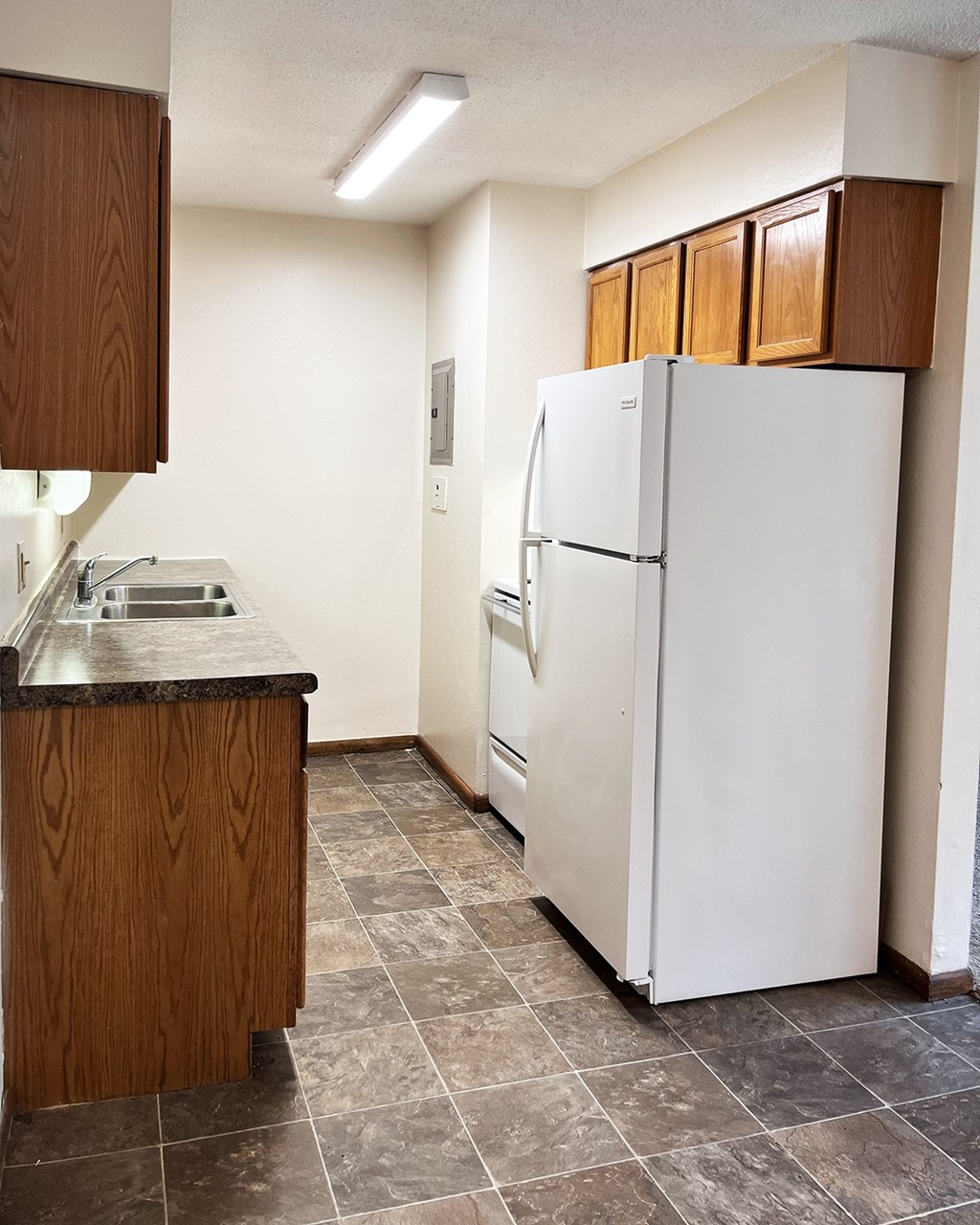 A white refrigerator in a kitchen with brown cabinets.