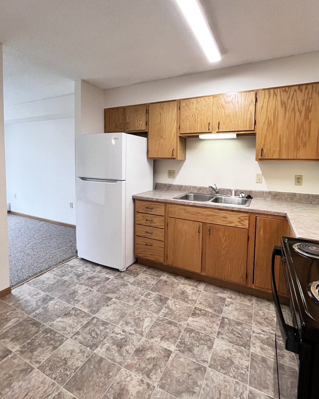 A kitchen with a white refrigerator, wooden cabinets, and a tiled floor.