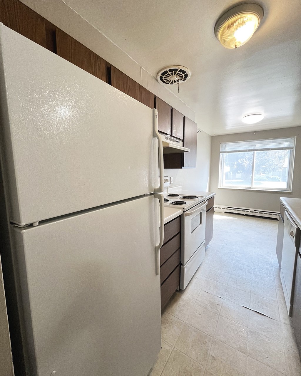an empty kitchen with a refrigerator and a window