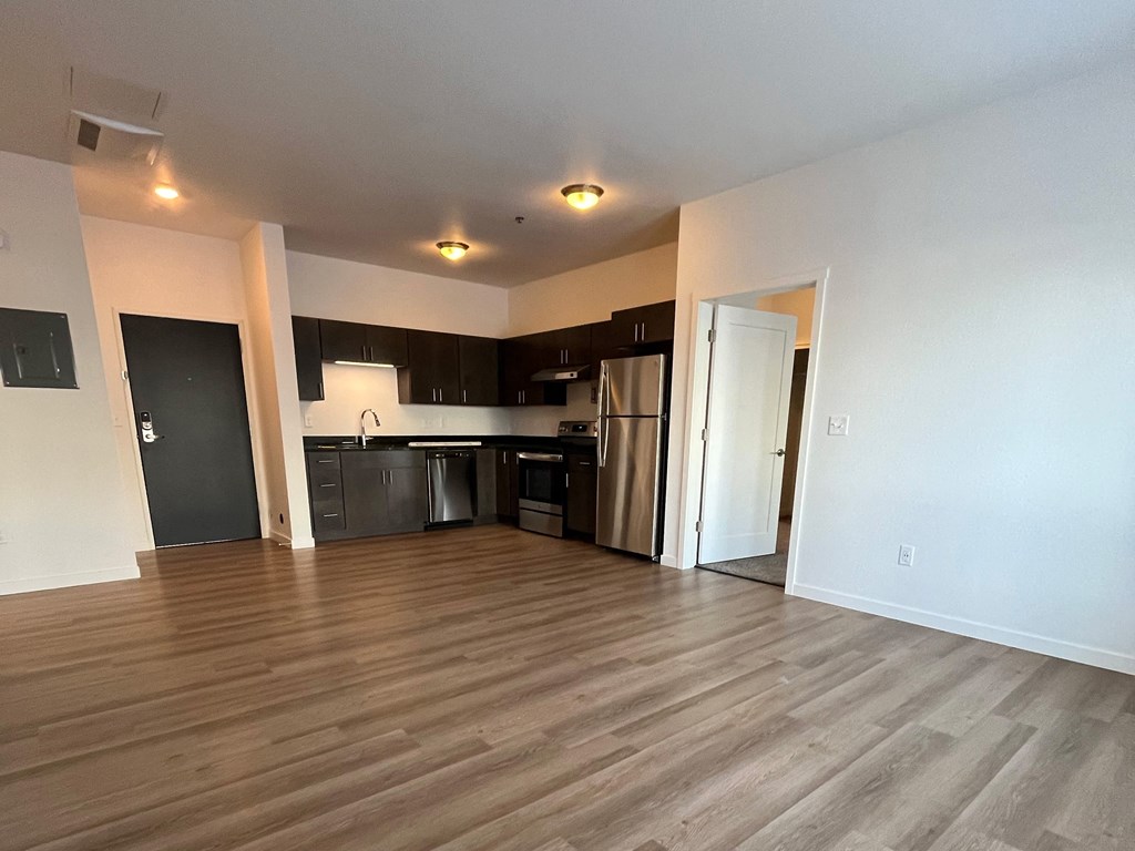 an empty living room with wood flooring and a kitchen