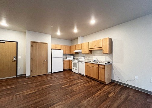 an empty kitchen with wood flooring and white appliances