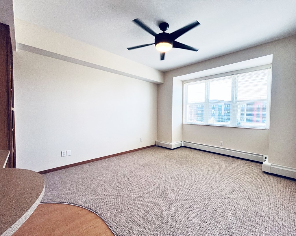 A room with a ceiling fan and a window overlooking a city.