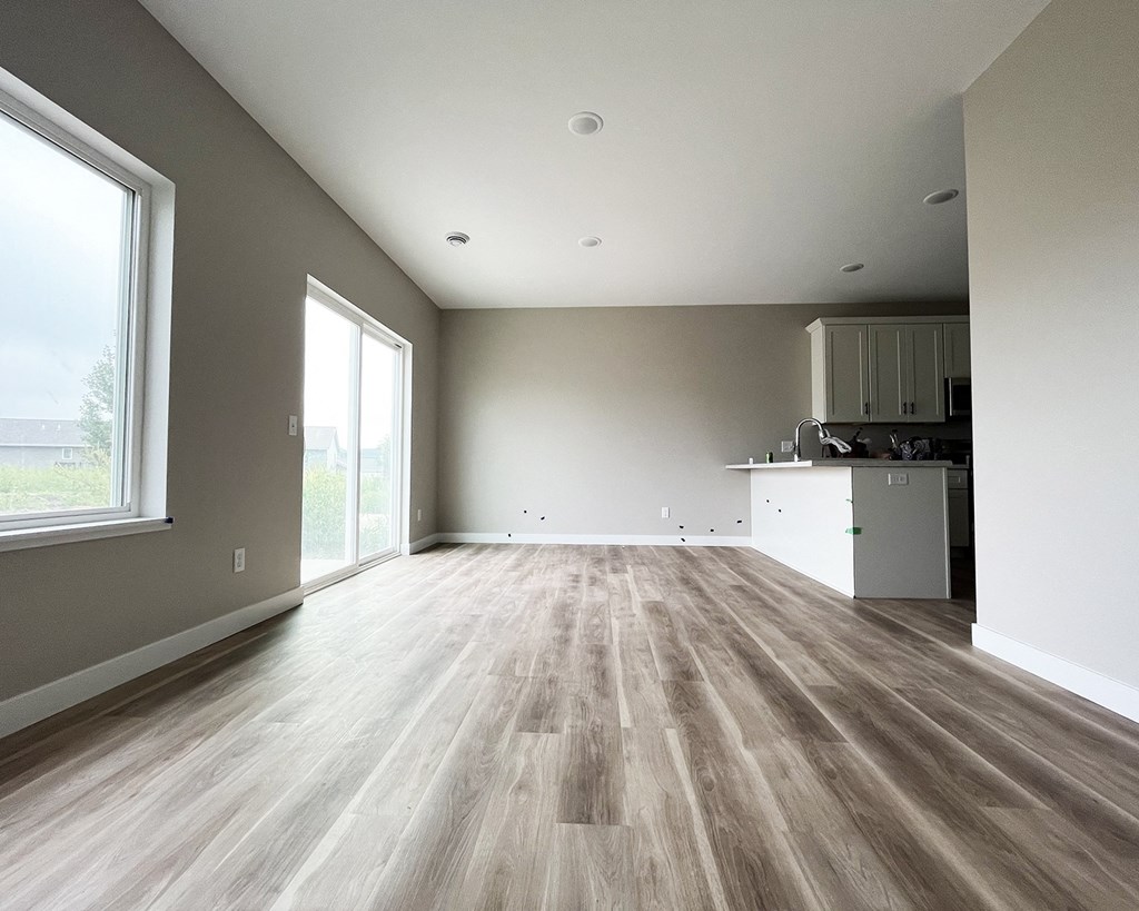 an empty living room with a kitchen in the background