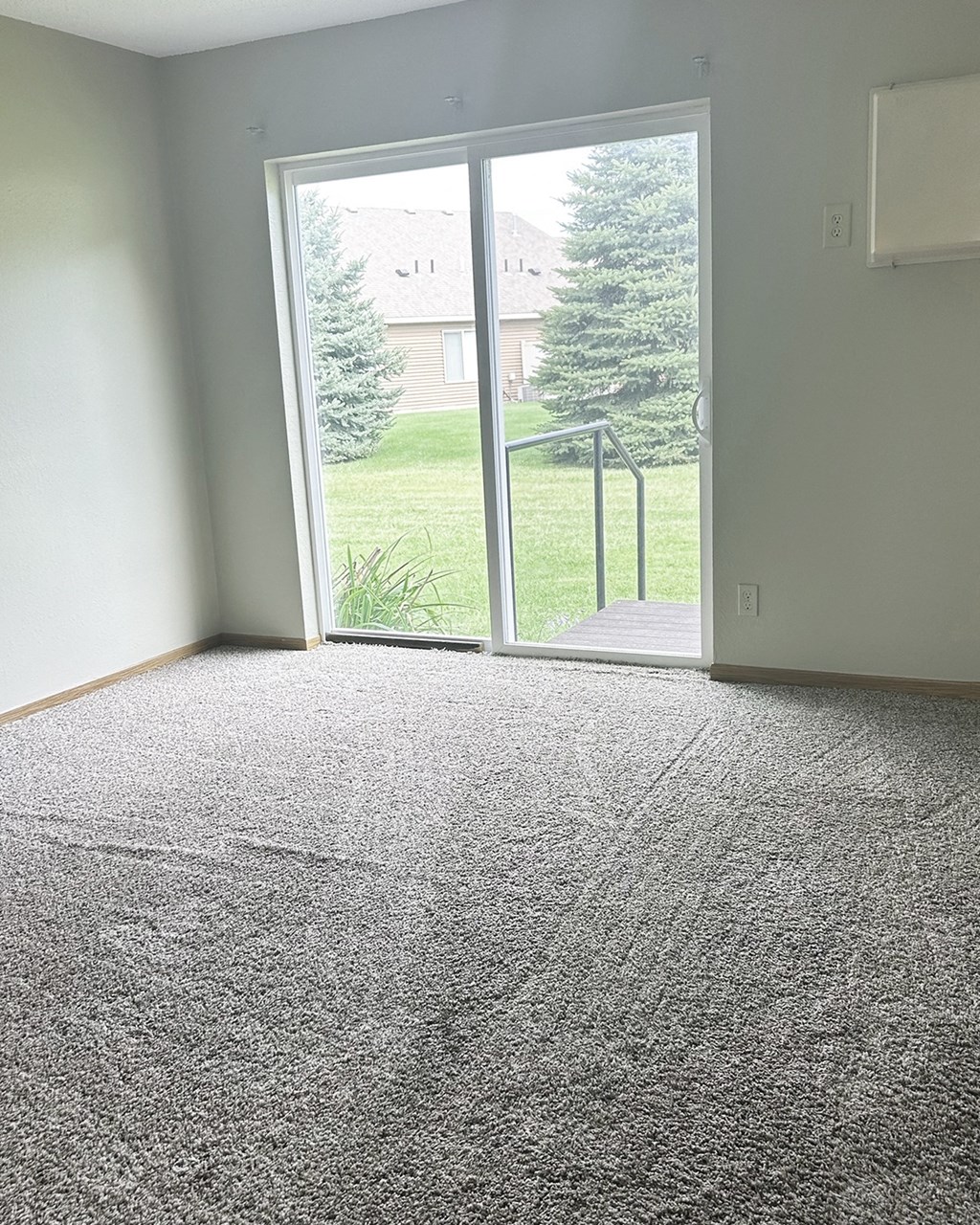 A room with a carpeted floor and a sliding glass door leading to a green lawn.