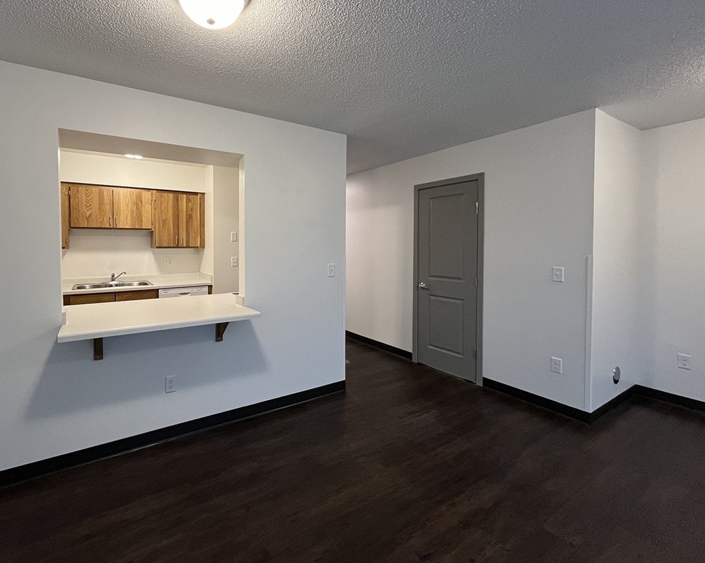 the living room and kitchen of an empty apartment with wood flooring and white walls