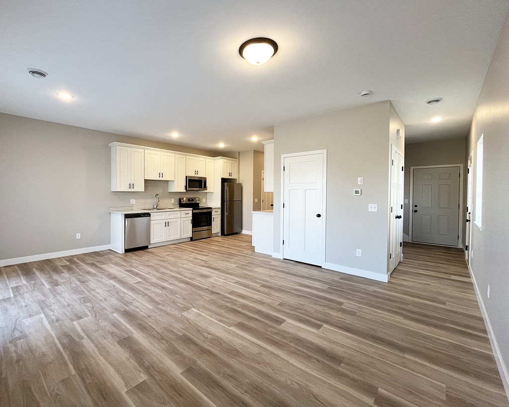 an empty living room and kitchen with wood flooring