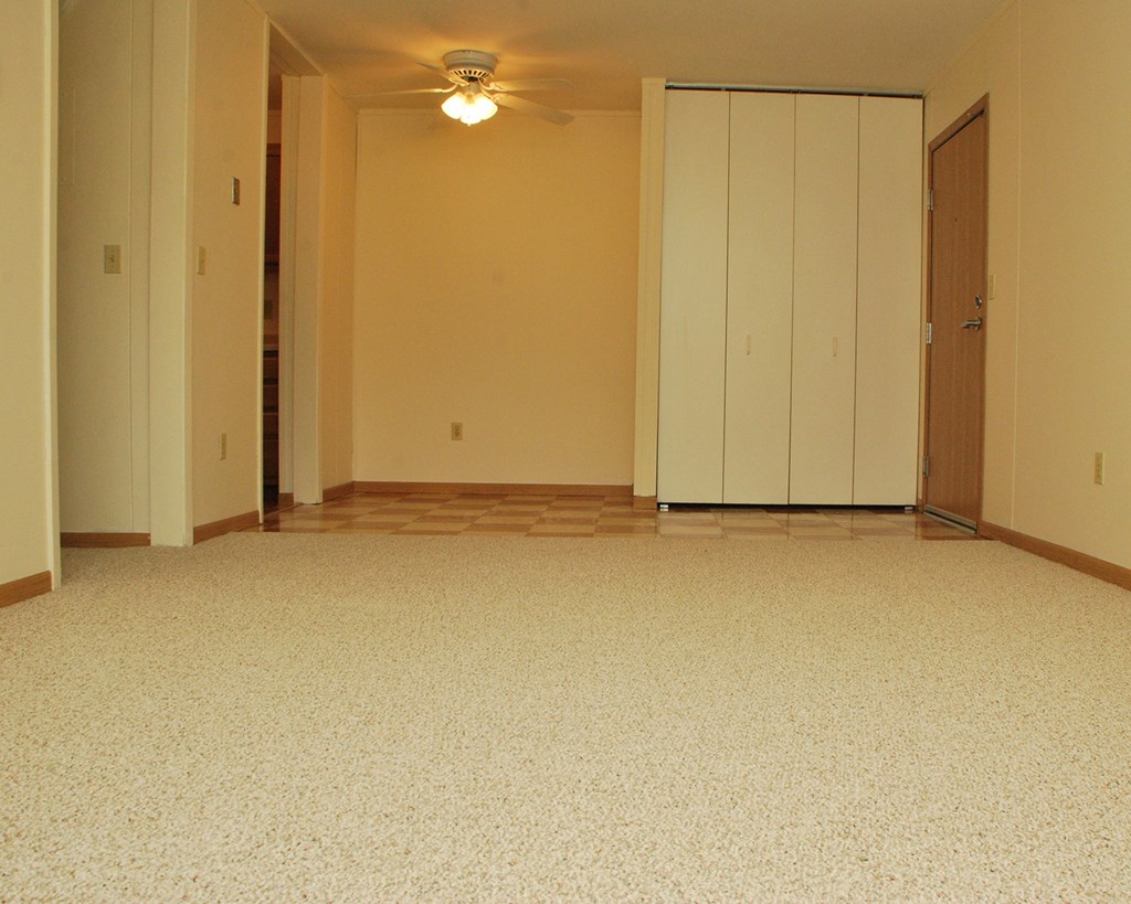 an empty living room with a ceiling fan and a closet