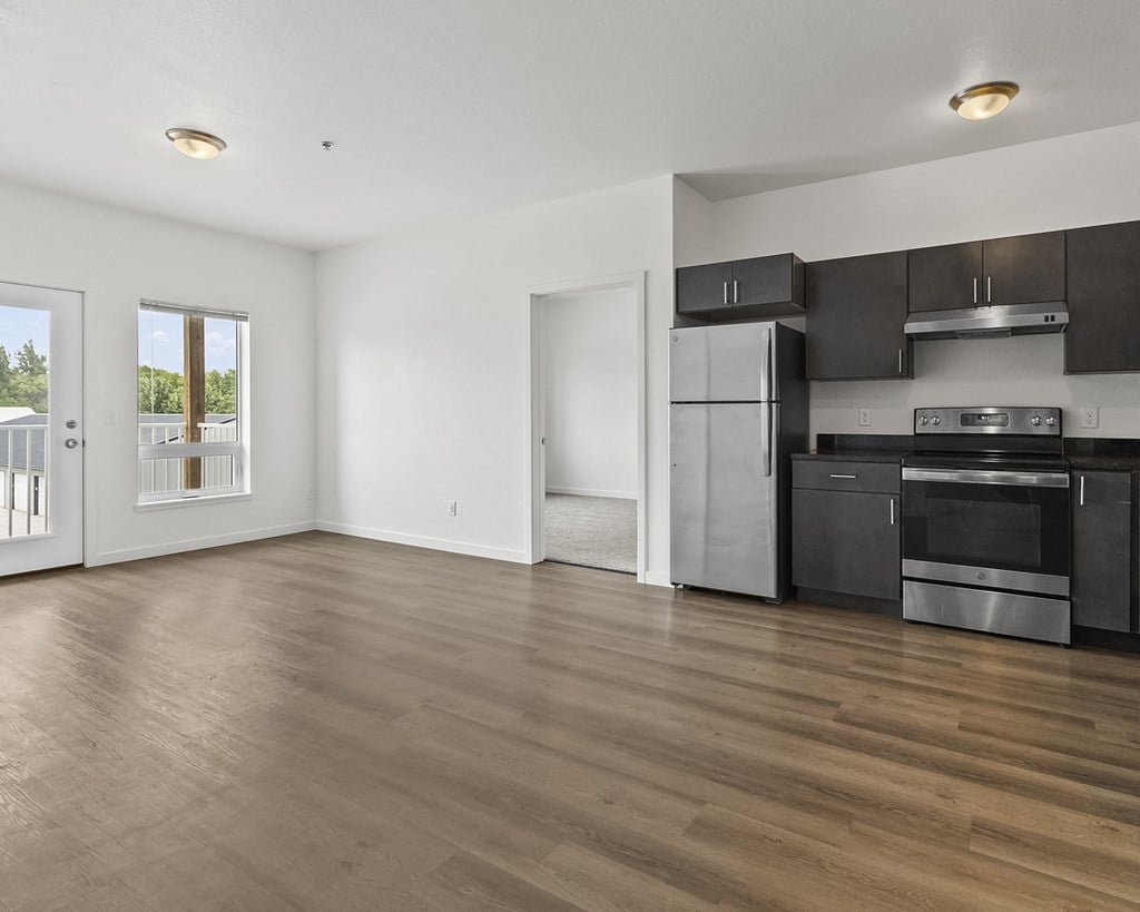 an empty living room with a kitchen and a door to a balcony