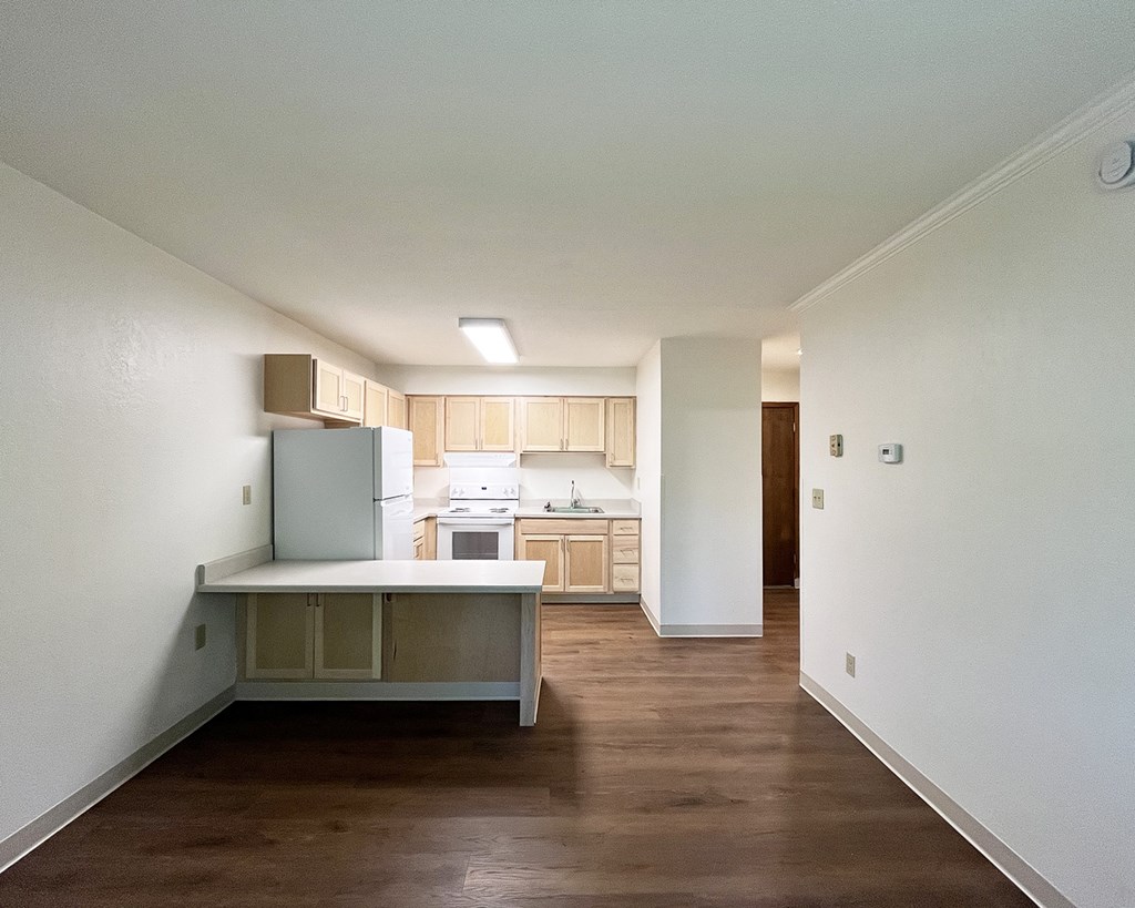 A kitchen with white walls and wooden floors.