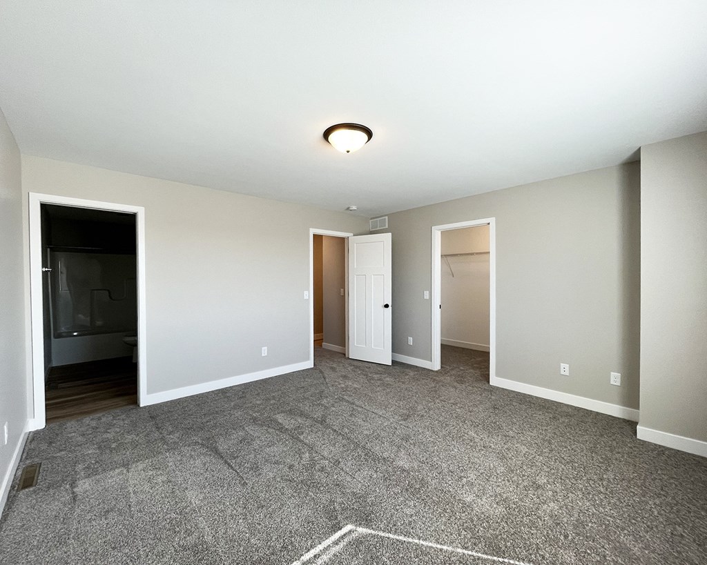 an empty living room with carpet and a door to a bedroom