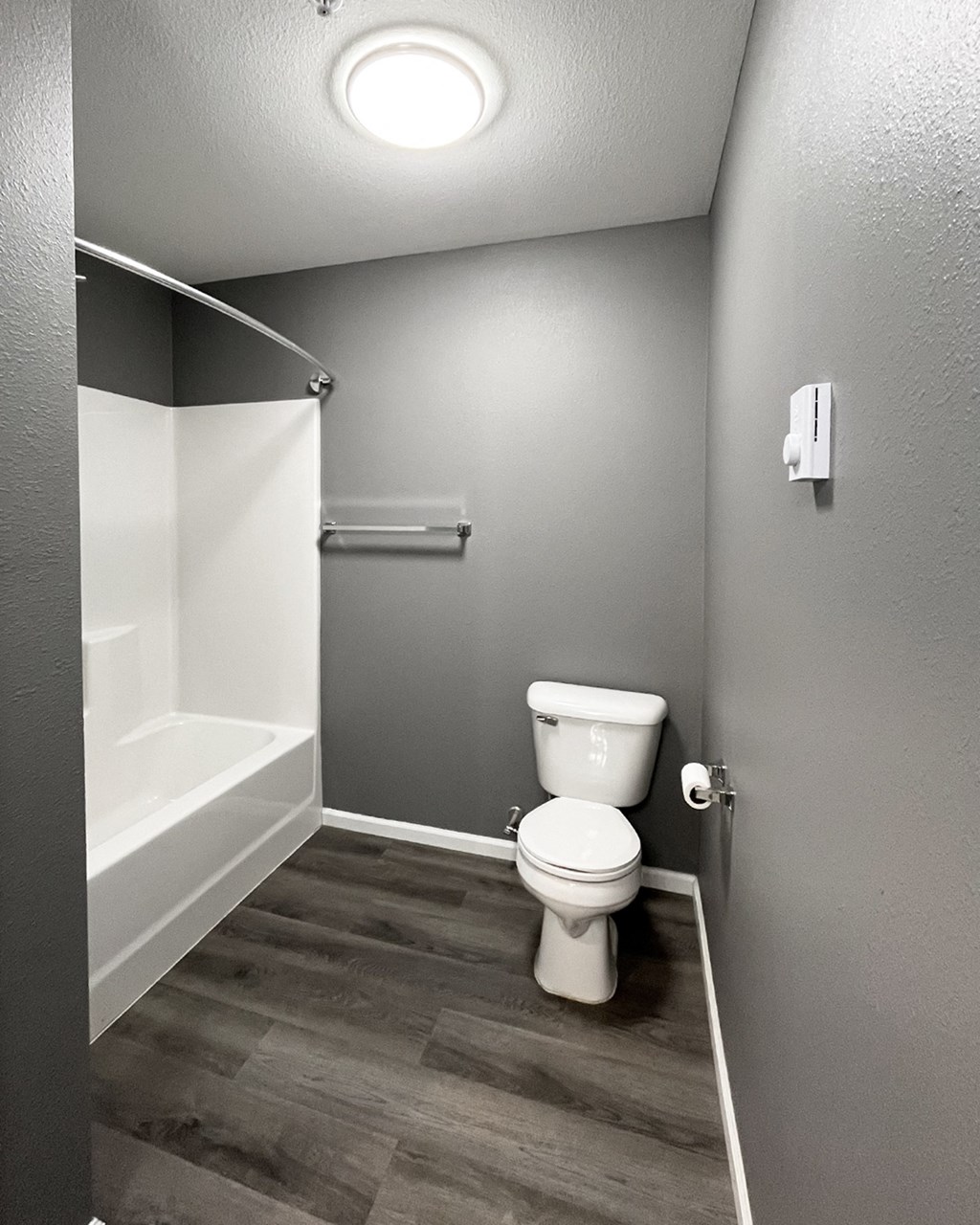 A white toilet in a small bathroom with a wood floor.