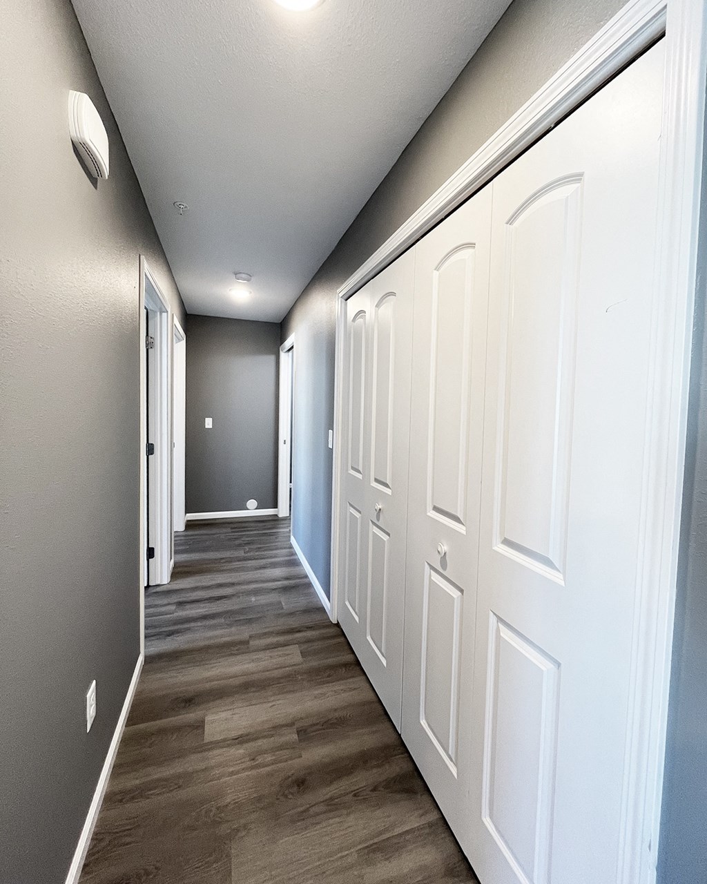 A long hallway with white doors on the right and a grey wall on the left.