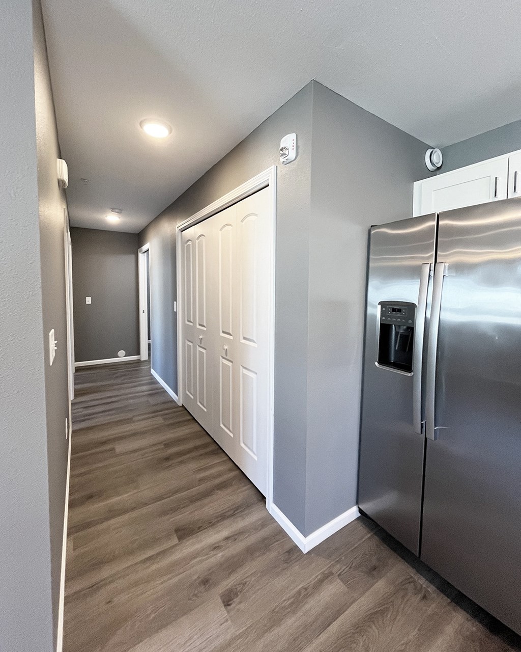 A long hallway with a stainless steel refrigerator on the right.
