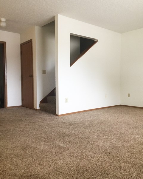 A room with a carpeted floor and a stairway leading to the second floor.