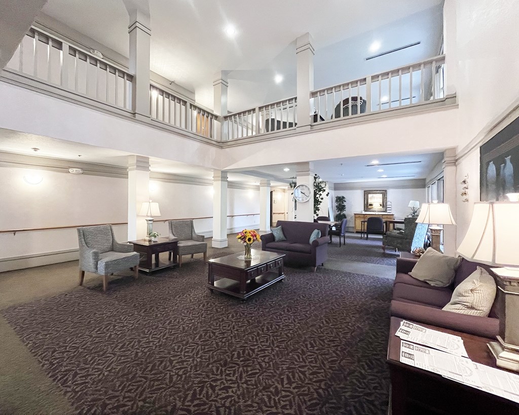 A large, well-lit living room with a carpeted floor and furnished with a sofa, armchairs, and a coffee table.