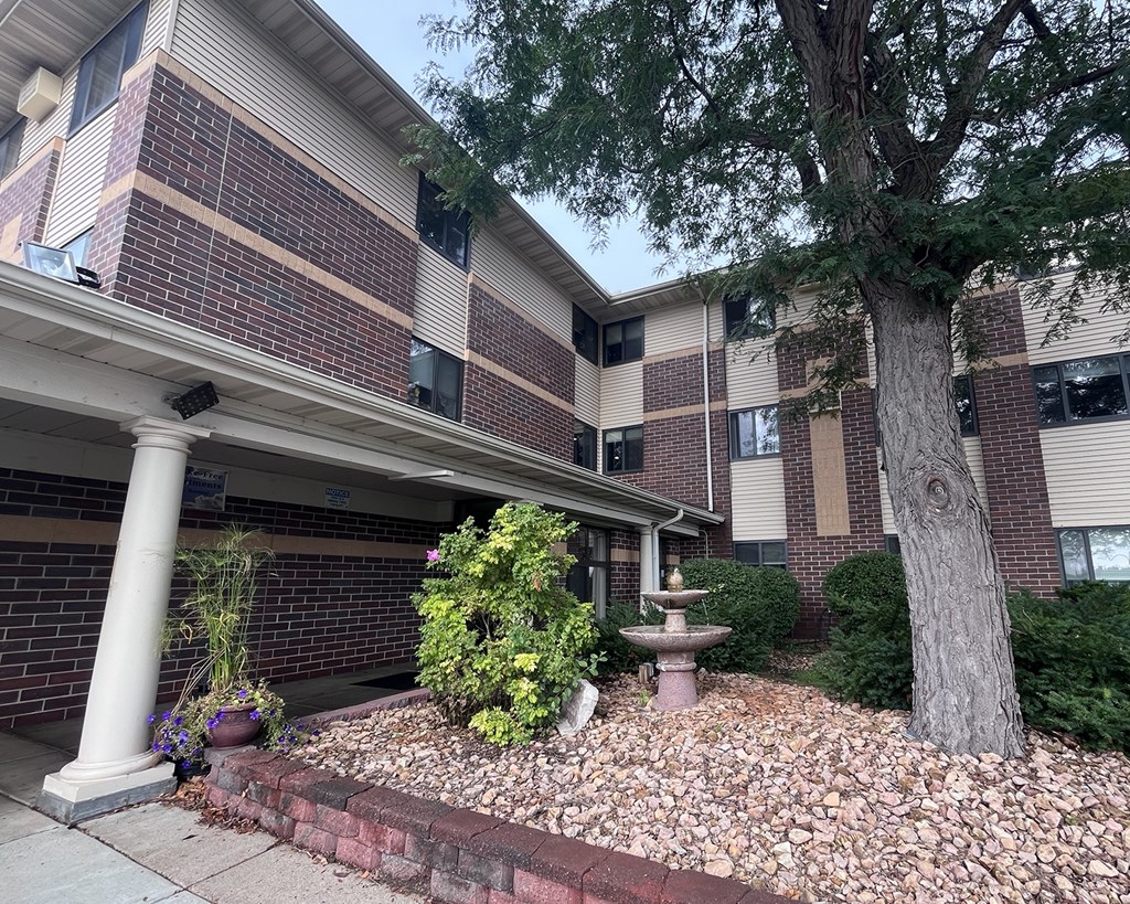 A tree in front of a building with a small fountain in the front yard.