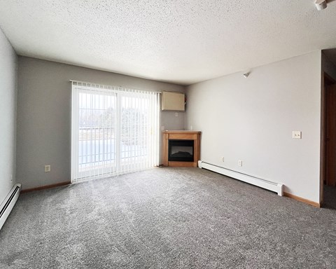 A sparsely furnished living room with a fireplace and sliding glass doors.