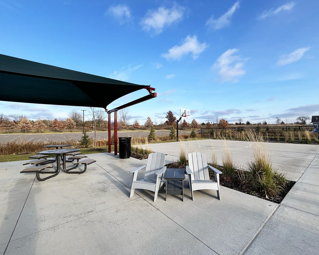 A patio area with a table, chairs, and a trash can under a shade structure.