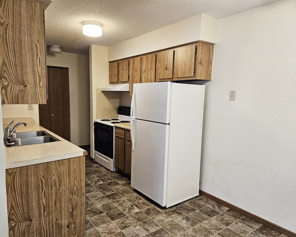 A kitchen with a white refrigerator, sink, and wooden cabinets.