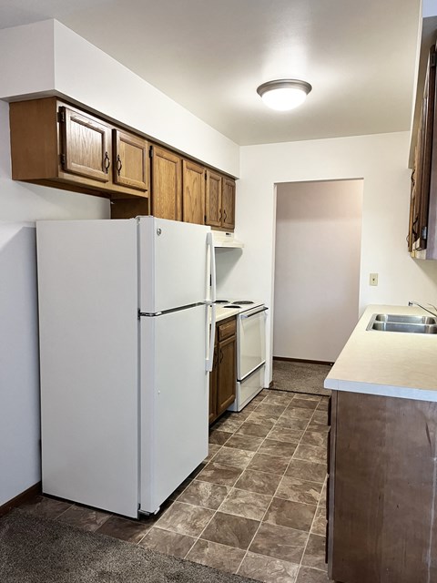 A kitchen with a white refrigerator and brown cabinets.