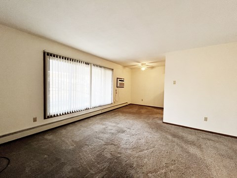 A room with a carpeted floor and a window with blinds.
