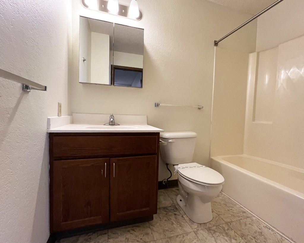 A white toilet sits in a bathroom next to a sink and a bathtub.