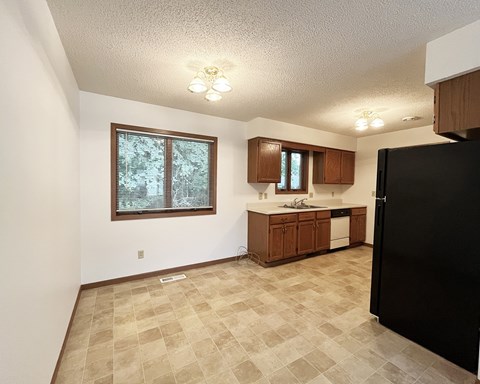 A kitchen with a black refrigerator and brown cabinets.