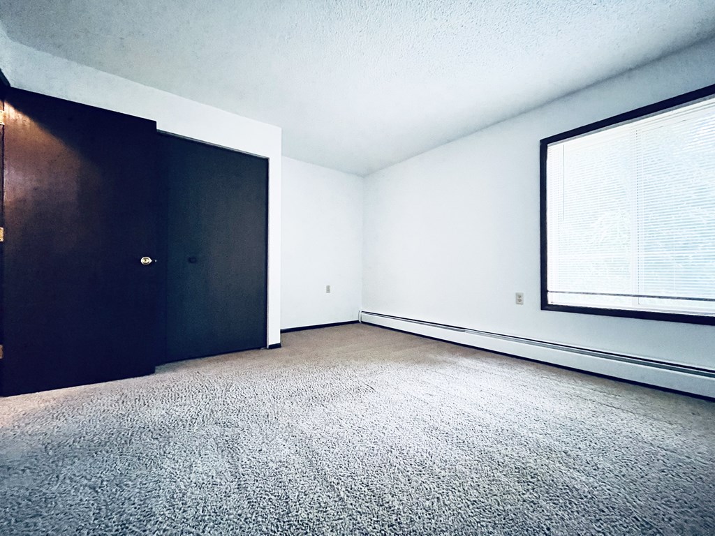 A room with a carpeted floor, a door, and a window with blinds.