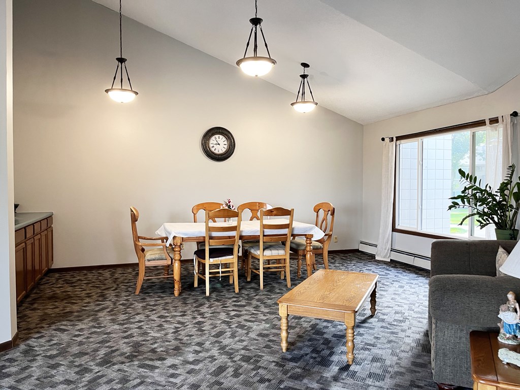 A dining room with a table set for six and a clock on the wall.
