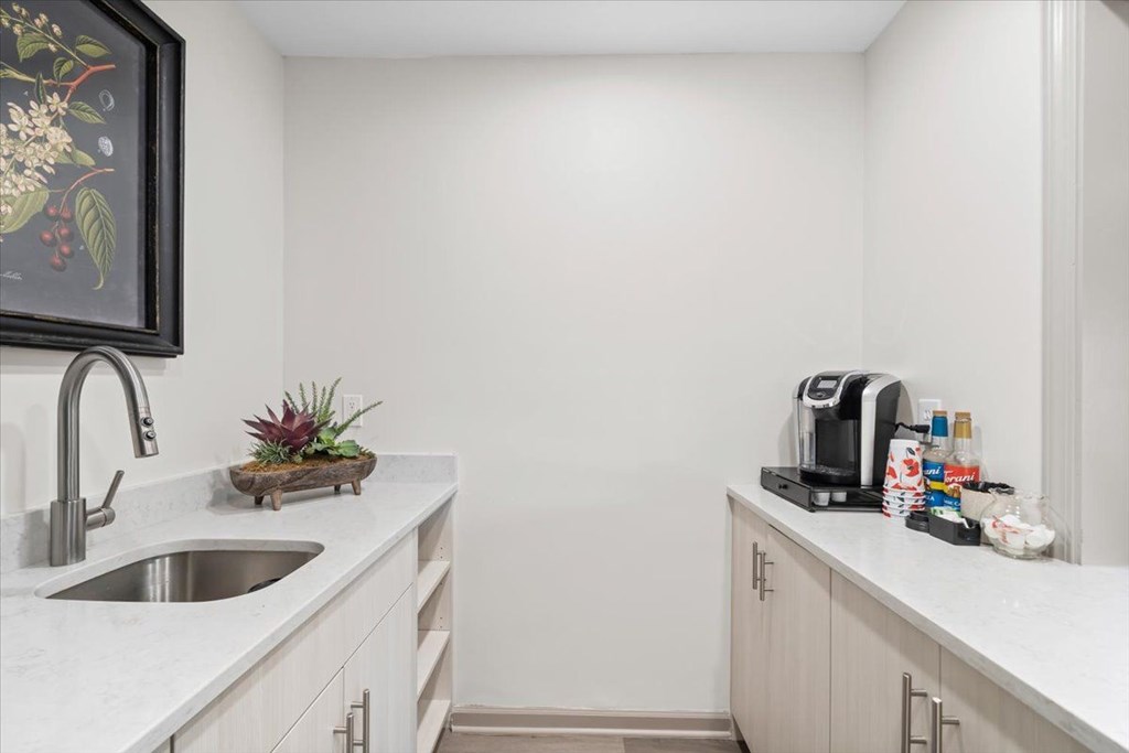 A kitchen with a sink, a coffee maker, and a framed picture on the wall.