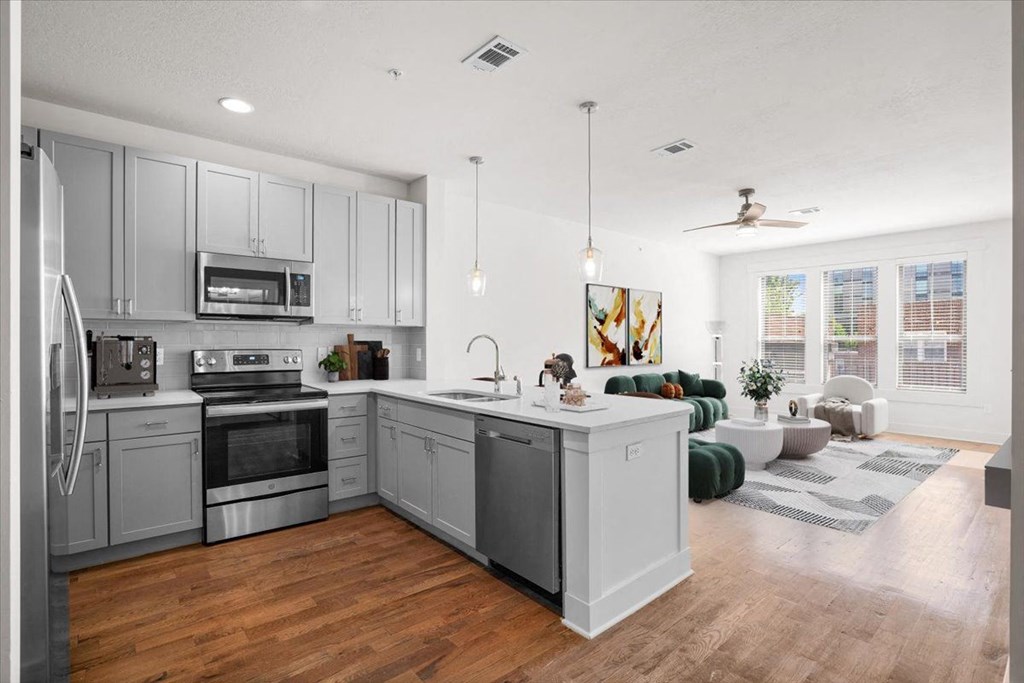 A large, open gourmet kitchen with stainless steel appliances including microwave and dishwasher, hardwood floors, and pendant lighting at Mirabelle Luxury Apartments, Kansas City