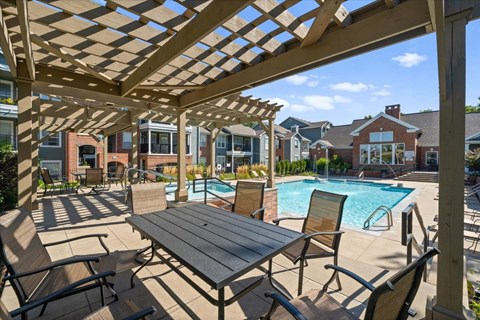 A wooden pergola over a table with chairs and a pool in the background. at Somerset Oaks Apartment Homes, Olathe 66062
