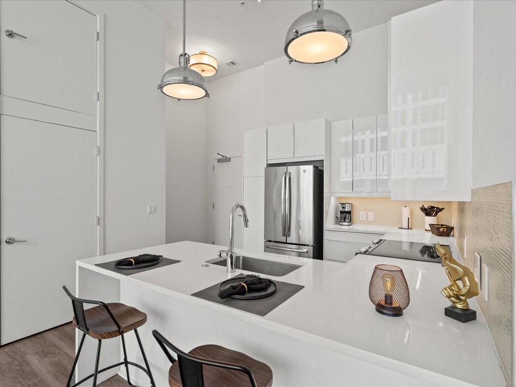a kitchen with white cabinetry and a large white island with a sink and two stools at Sky On Main Apartments, Missouri City