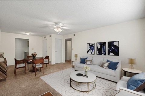 A living room with a dining space, a ceiling fan, and a hallway closet.