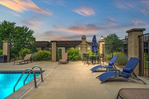 a swimming pool with blue chairs and umbrellas    and a fence at Deerfield Apartments, Kansas