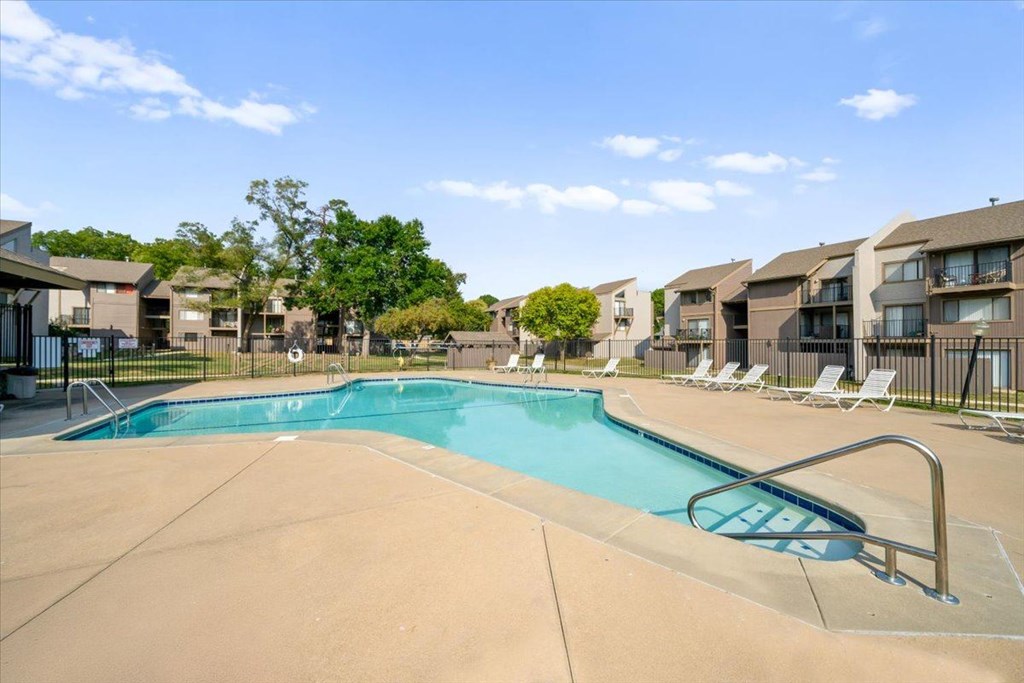 A swimming pool surrounded by lounge chairs and apartment buildings.