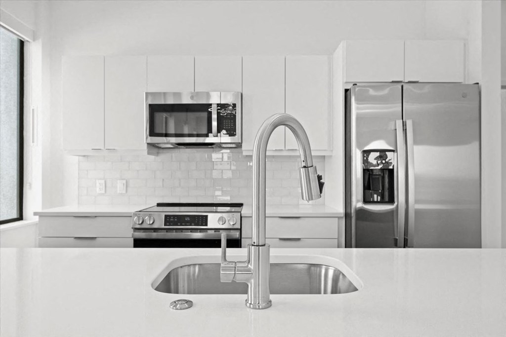 a white kitchen with stainless steel appliances and a sink at Sky On Main Apartments, Missouri City, MO