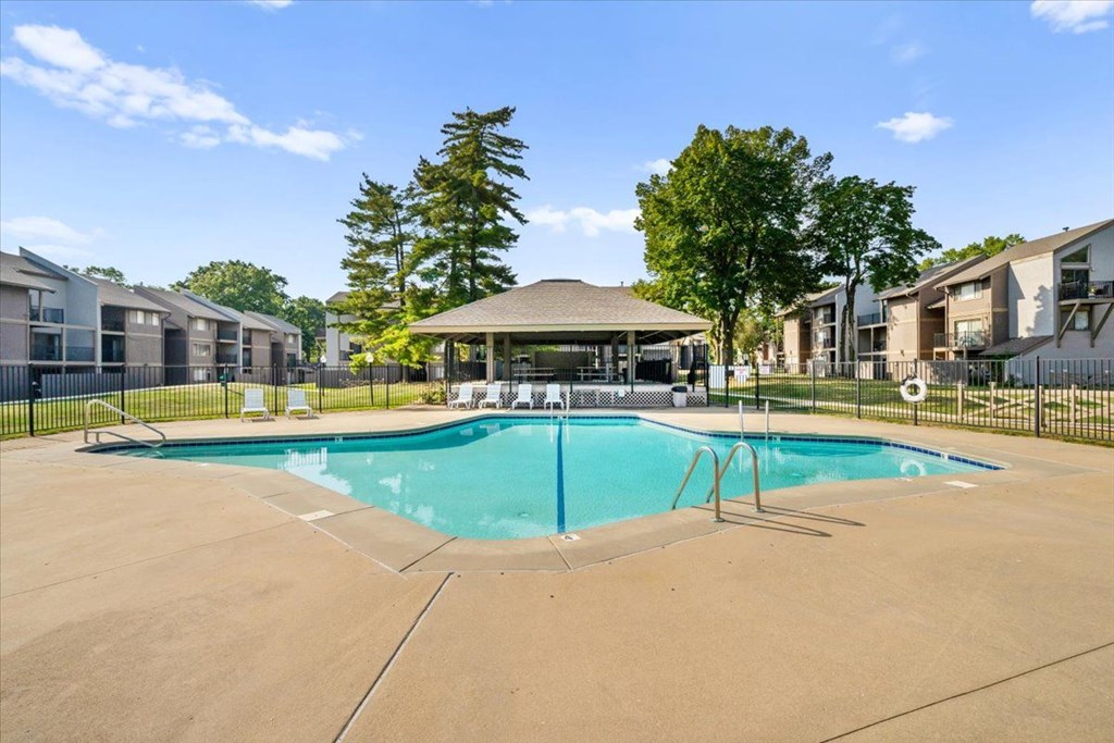 A swimming pool surrounded by a fence and trees with a building in the background.