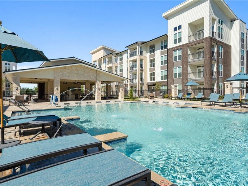 a swimming pool with tables and chairs next to an apartment building