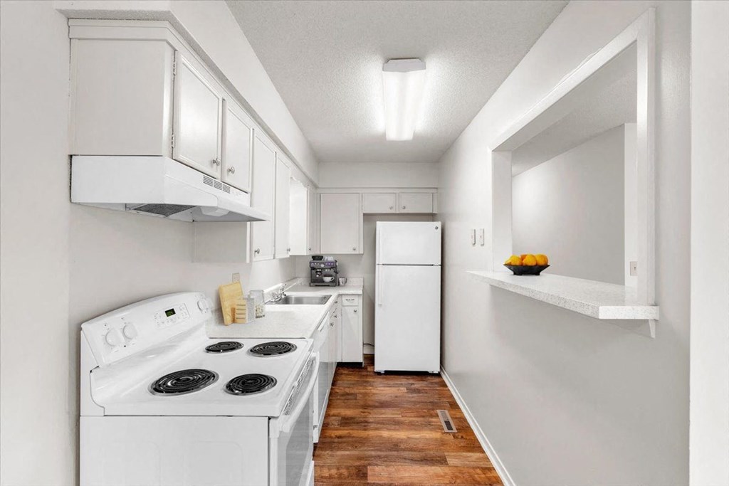 A kitchen equipped with a dishwasher, range with stove and oven, refrigerator, and hardwood floors.