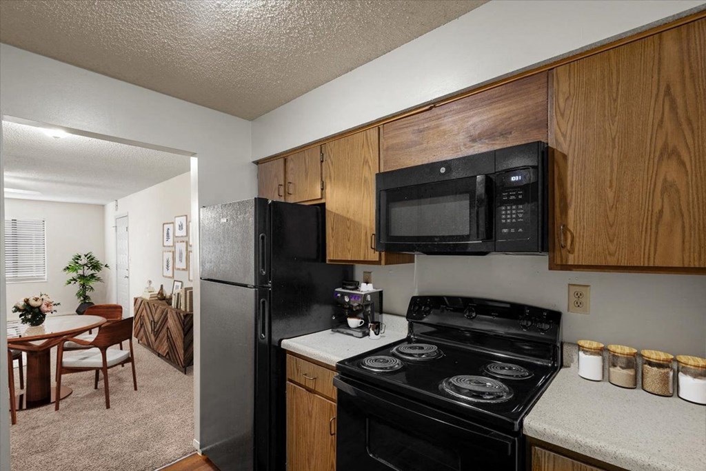 A kitchen with black appliances, wooden cabinets, and white countertops with a doorway to the dining area at Bristol Pointe Apartment Homes, Kansas