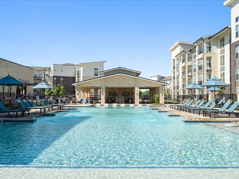 a large swimming pool with lounge chairs and an apartment building