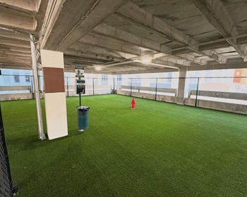 Covered dog park with artificial turf, a red fire hydrant, a bench, and a waste station inside the parking garage at SKY on Main Apartments in Downtown Kansas City, MO.
