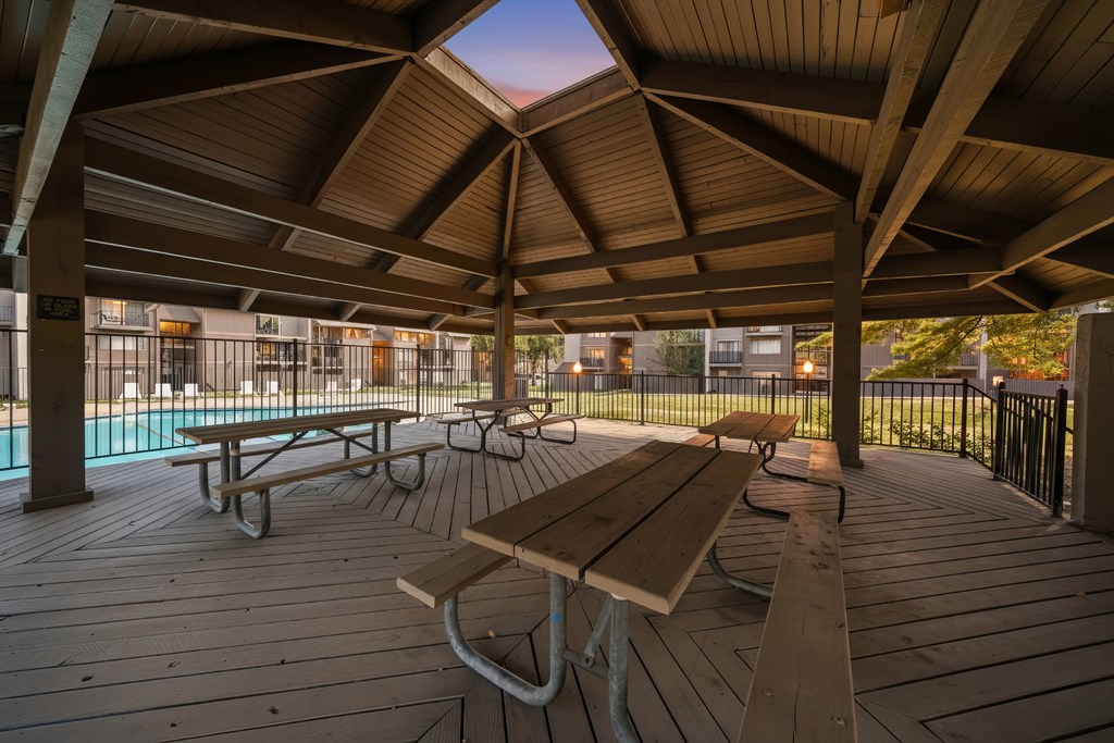 A wooden deck with picnic tables and a pool in the background.