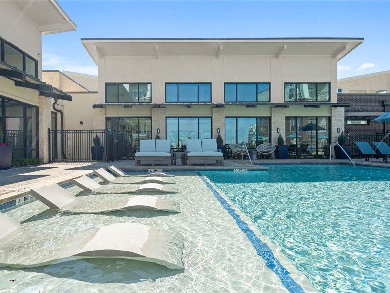 a large swimming pool with lounge chairs in front of a house