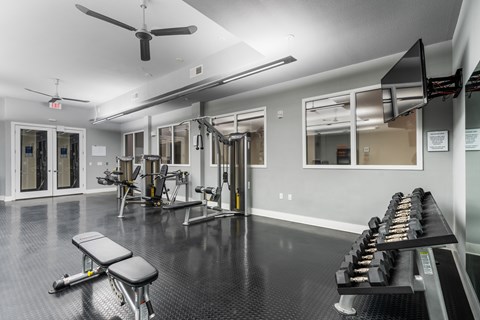 Free weights, strength machines, and mounted TV in fitness center at West 39th Street Apartments.