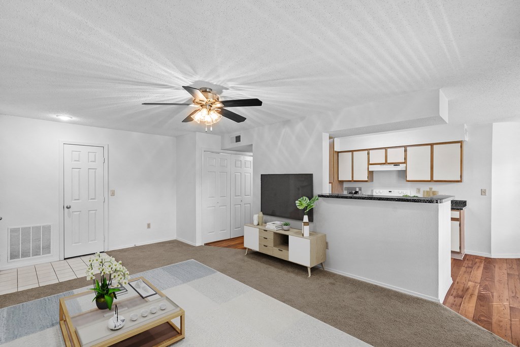 a living room with a ceiling fan and a kitchen in the backgroundat Stonebriar Apartments, Overland Park, KS